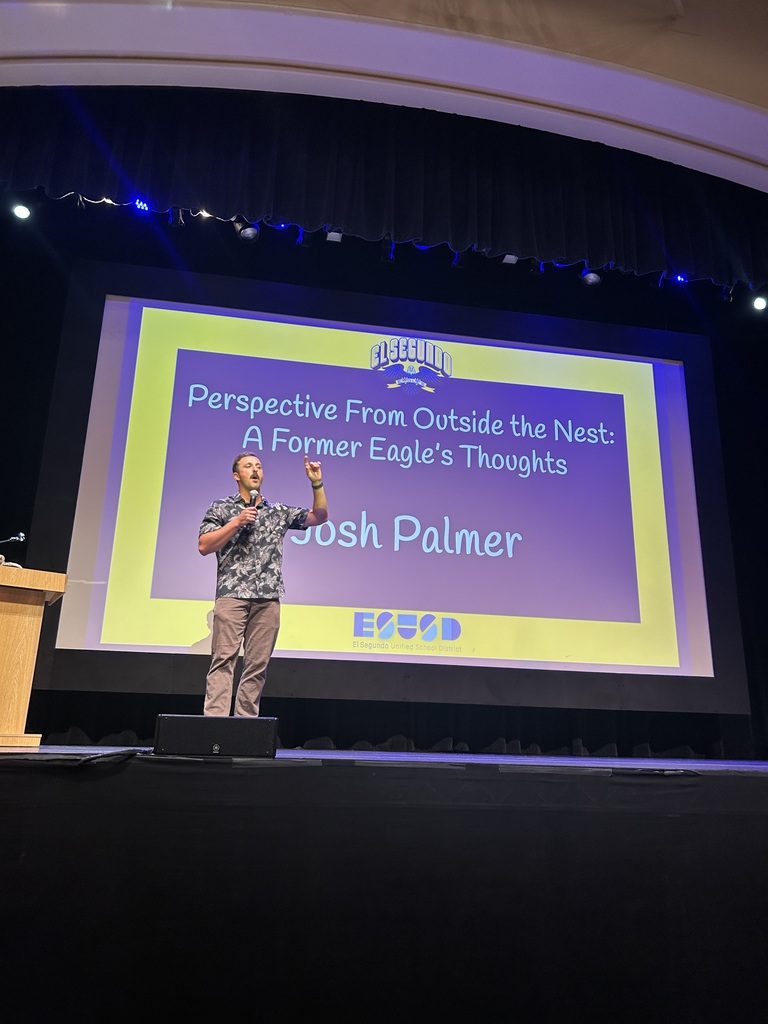 Speaker Josh Palmer stands on stage with a microphone, gesturing while addressing the audience. Behind him, a large screen displays the presentation title: 'Perspective From Outside the Nest: A Former Eagle’s Thoughts,' along with the El Segundo Unified School District logo.