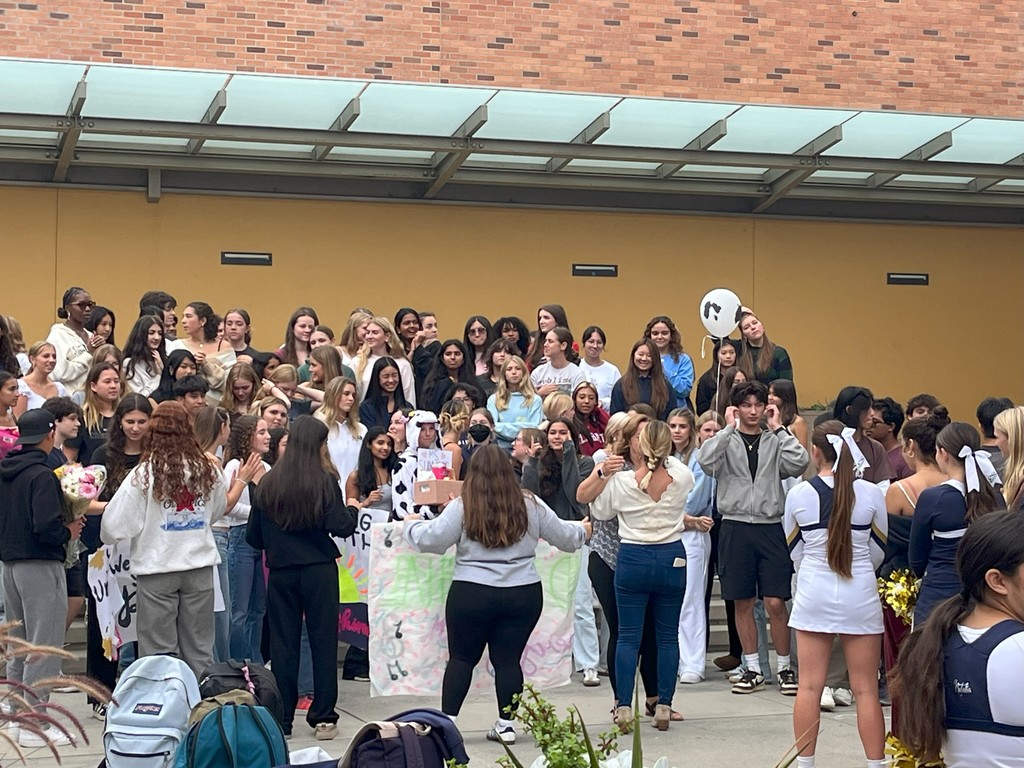 A large group of students gather on steps outside, holding balloons and signs in support of Ms. Summers