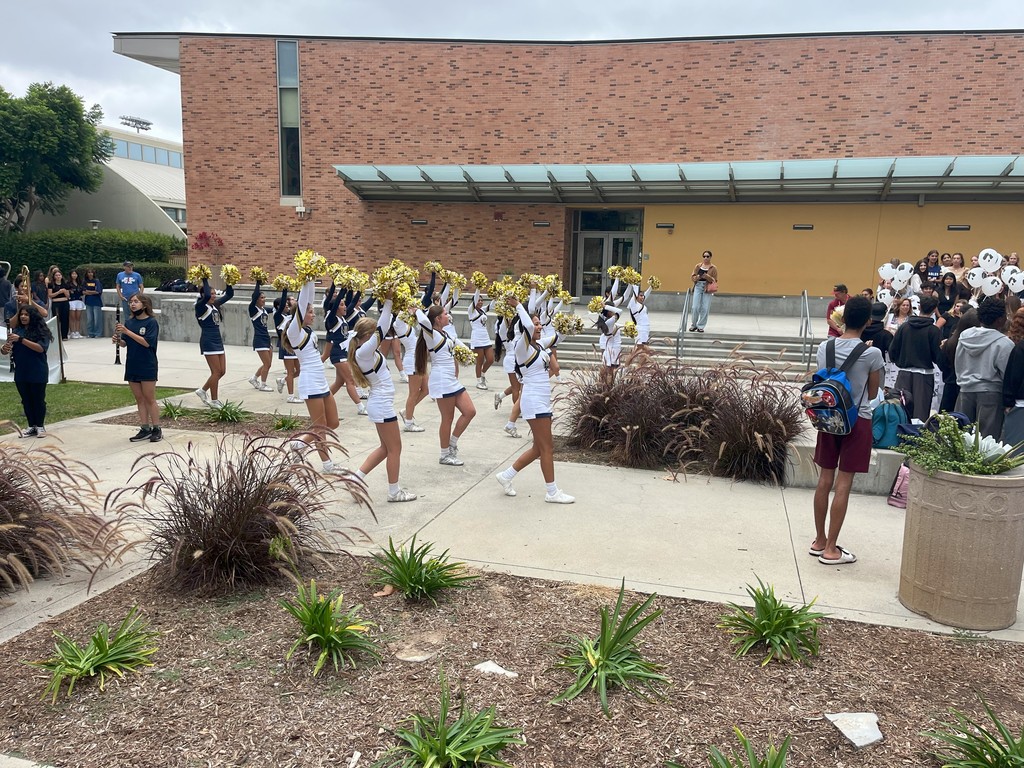 Cheerleaders in white uniforms with gold pom-poms perform in formation