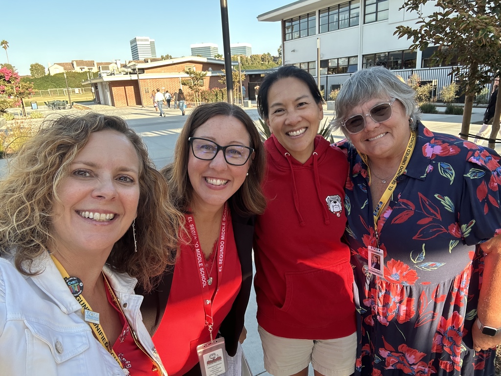 Four women stand outside on campus smiling for a group selfie