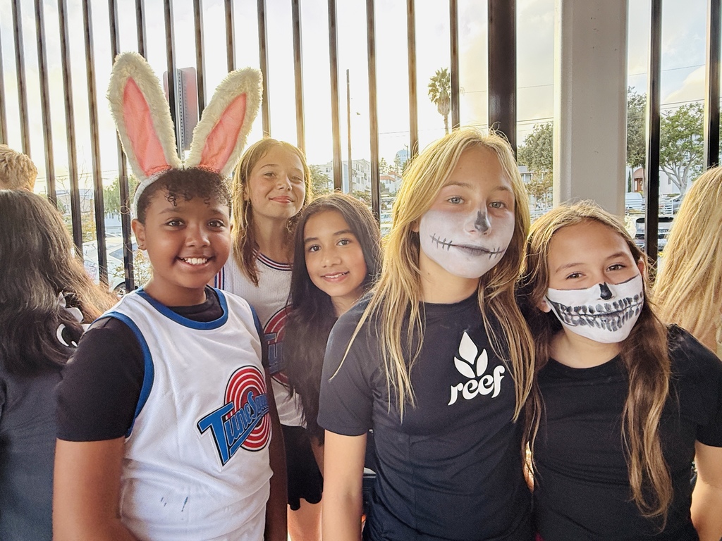 Five students wearing Halloween face paint and bunny ears smile for a photo in front of a metal fence at sunset.