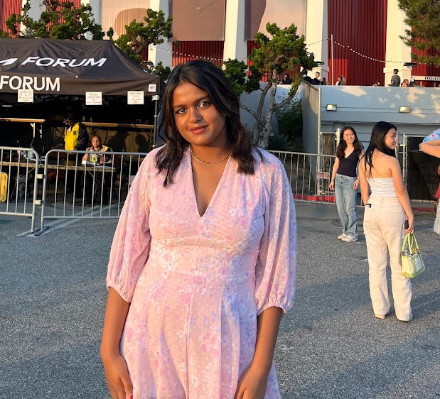 Abhaya Alurkar wearing a light pink dress stands outdoors in front of The Forum event venue