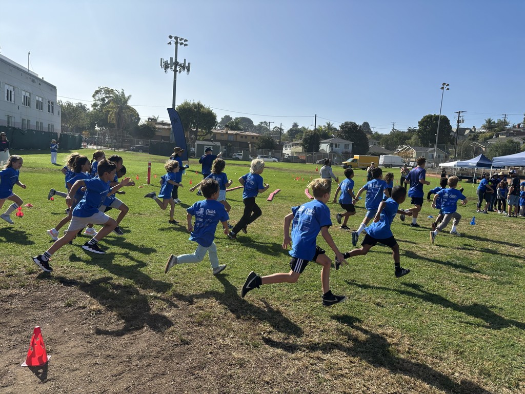Children wearing matching blue event shirts sprint across a grassy field