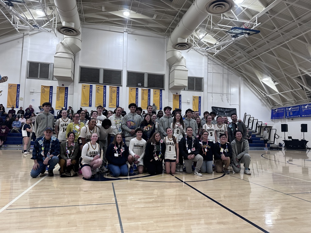 Large group of students and staff pose together on a gym floor, celebrating in front of bleachers and school banners.