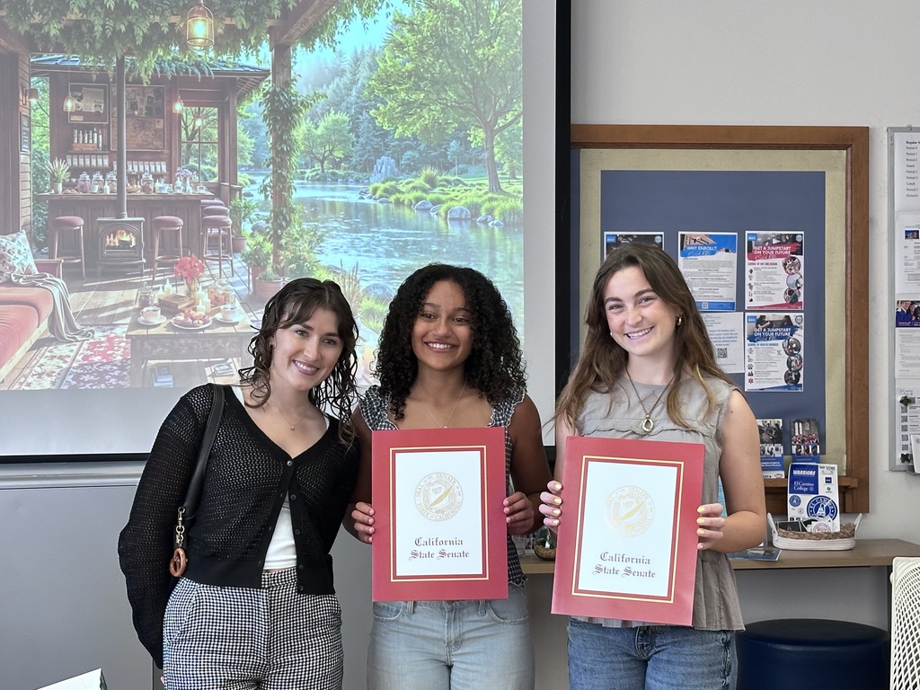 Three smiling students stand together, two holding California State Senate certificates in a classroom setting.