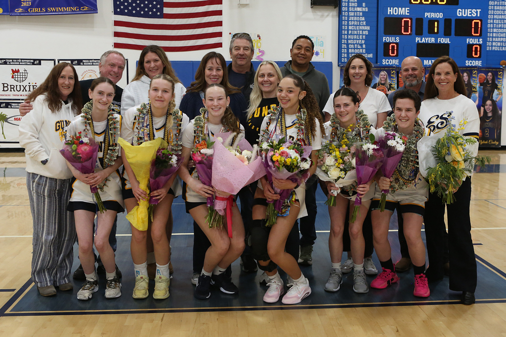 High school girls' lacrosse team posing with bouquets and leis on gym court during senior night celebration