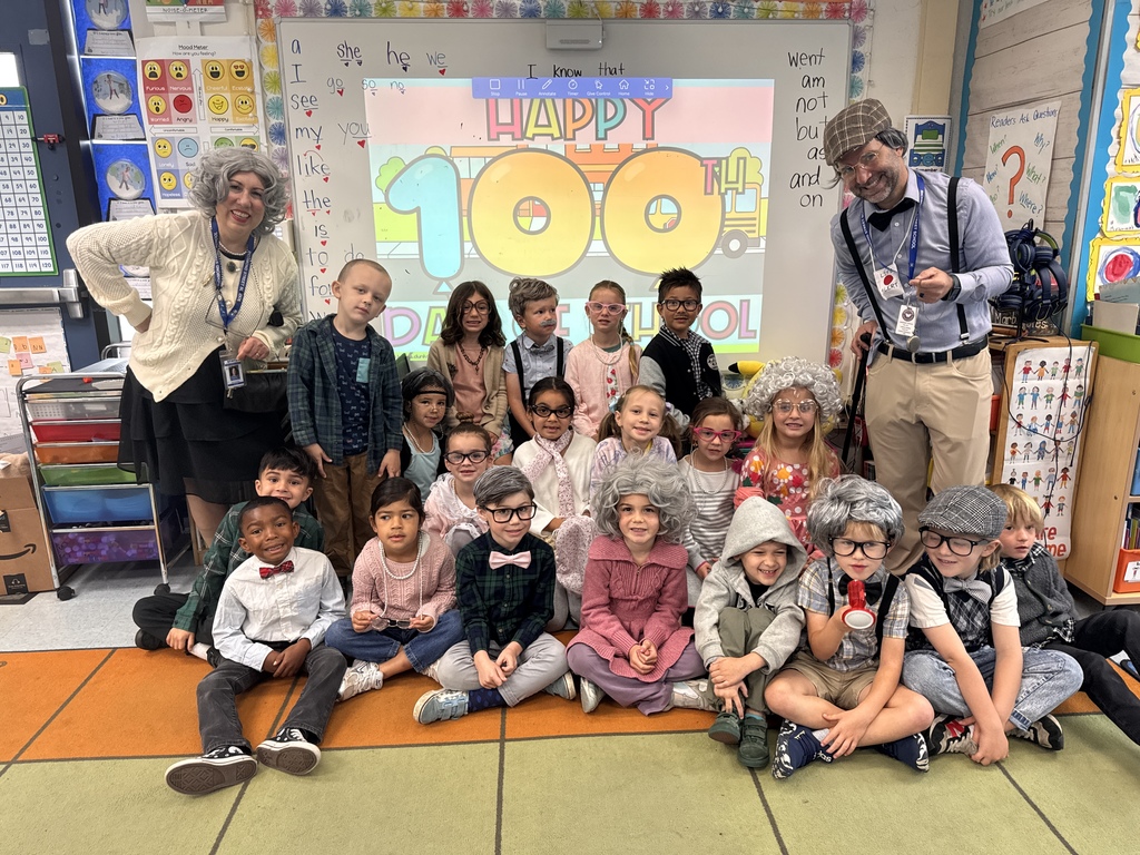 Students and teachers celebrate the 100th day of school, dressed as if they are 100 years old, posing together in the classroom.