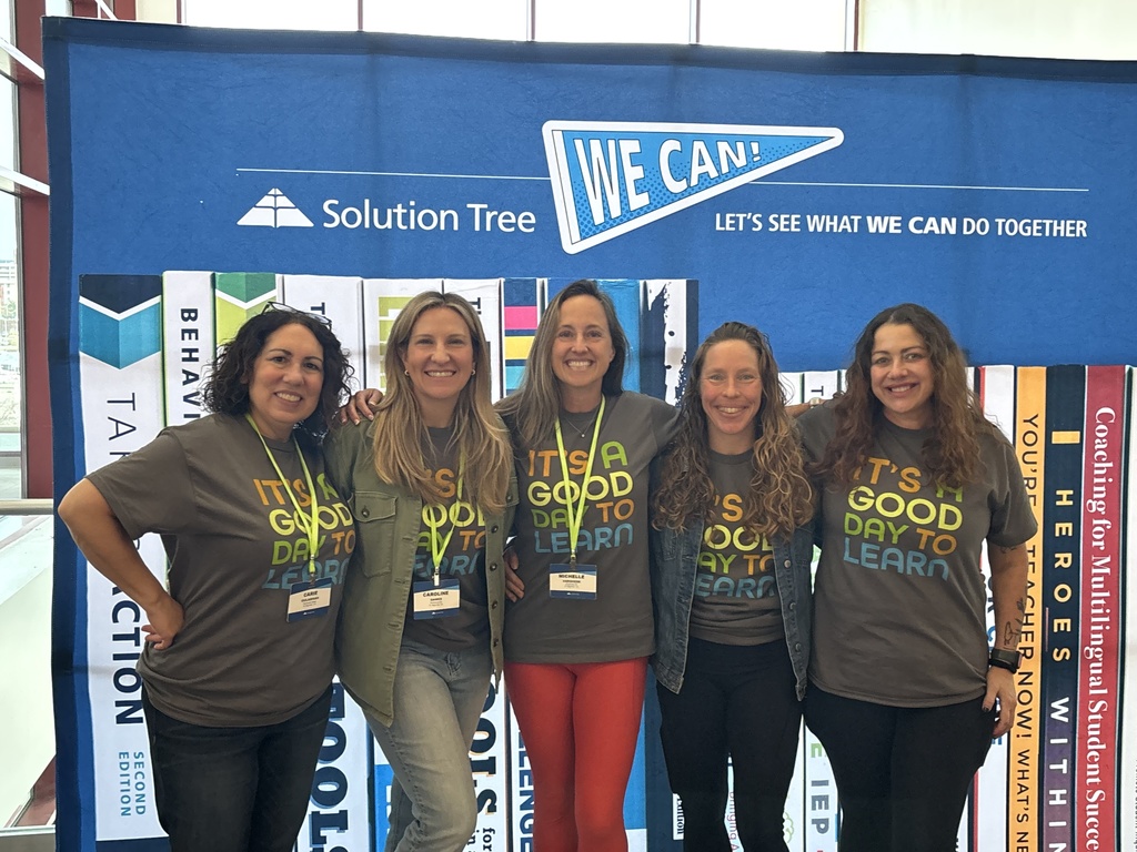 Five educators standing together and smiling in front of a “Solution Tree – We Can! Let’s See What We Can Do Together” display, wearing matching shirts that read “It’s a Good Day to Learn.”