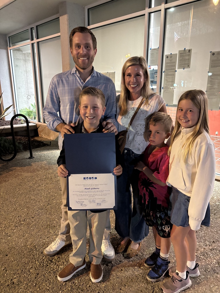 Family of five standing outside a building at night, with one child holding a certificate of achievement.