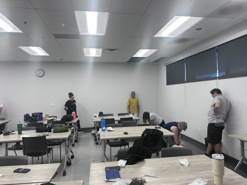 Adults spread across a classroom practice CPR on mannequins while others observe near the walls.