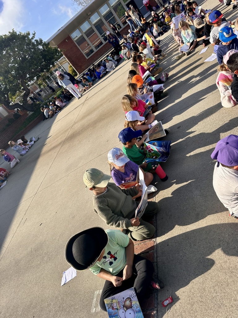 Students sit in long rows outside on a sunny day, reading books together during a school-wide reading activity.