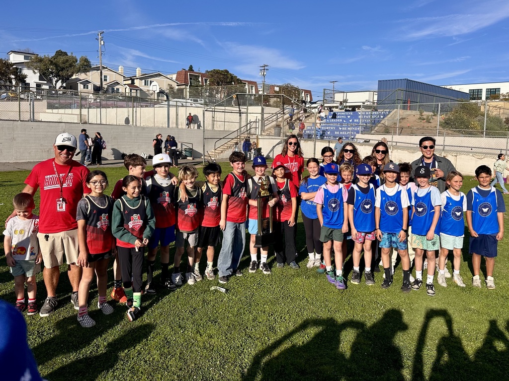 Two youth teams and coaches stand together on a field, smiling with a trophy after a school sports game.
