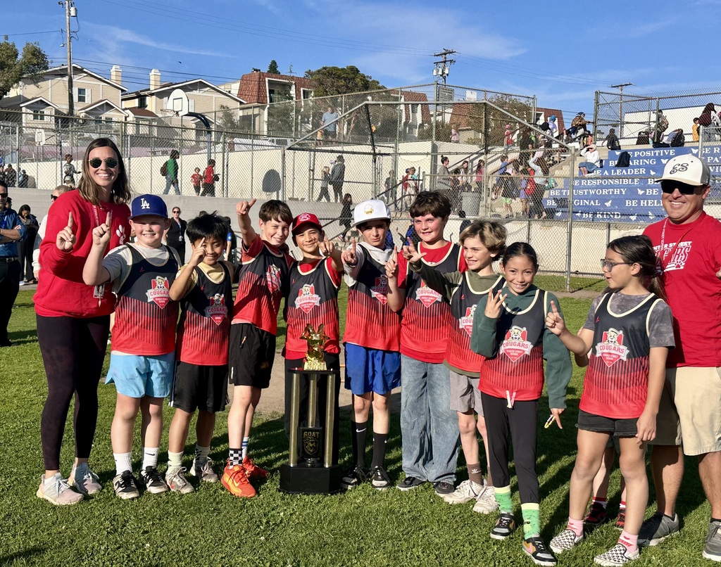Students in red team jerseys pose with a trophy and coaches, holding up fingers to celebrate their win.