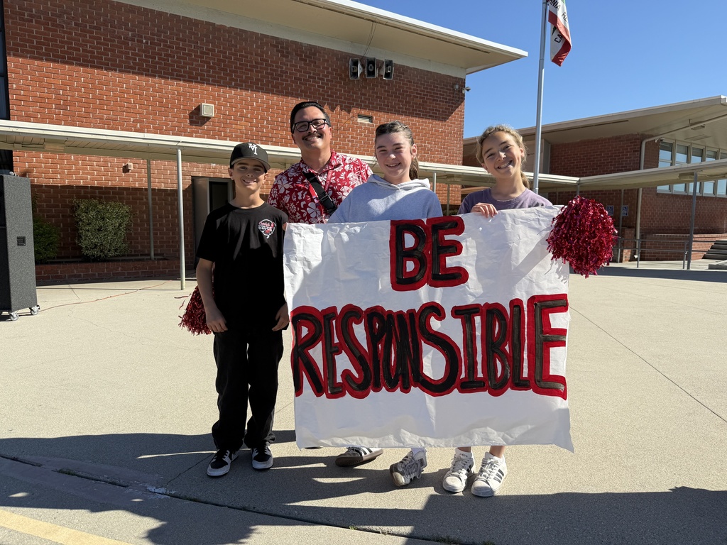 Three students and an adult hold a sign reading “Be Responsible” while standing outside on a sunny school campus.