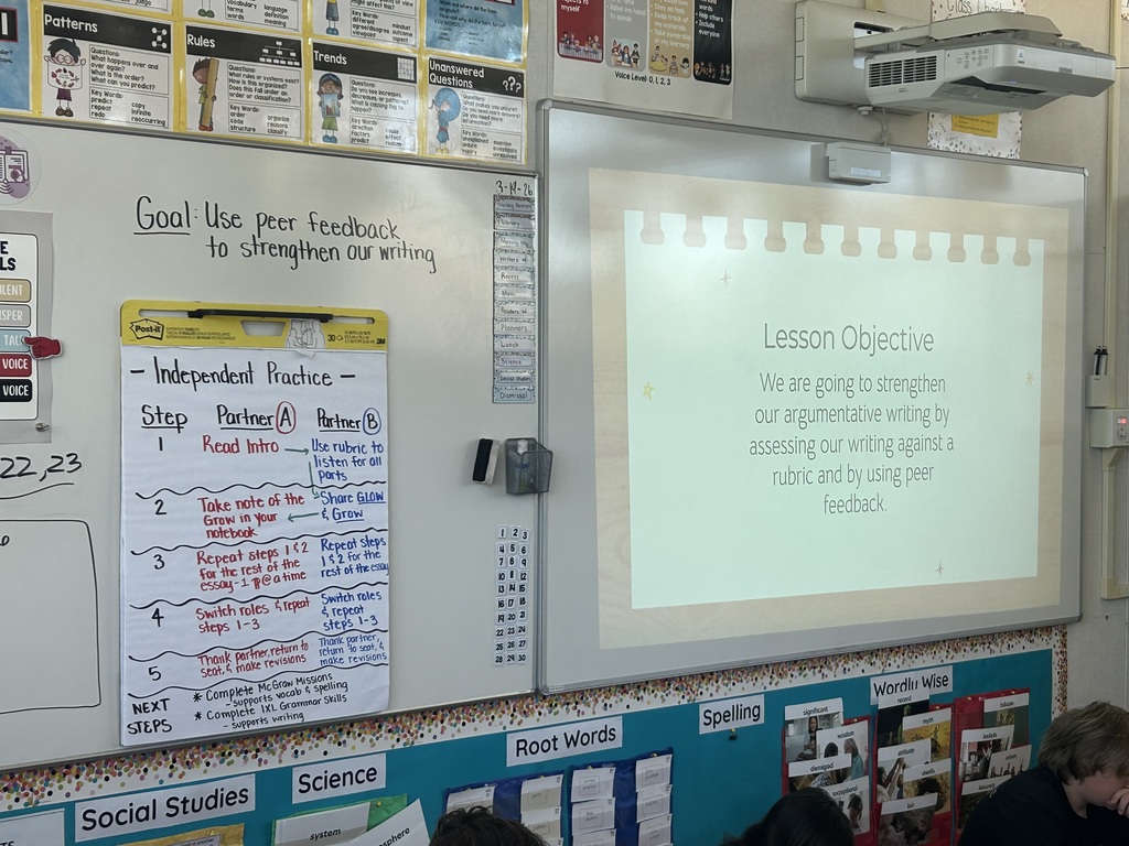 Classroom whiteboard shows writing lesson on peer feedback, with steps for partner review and a projected objective about strengthening argumentative writing.
