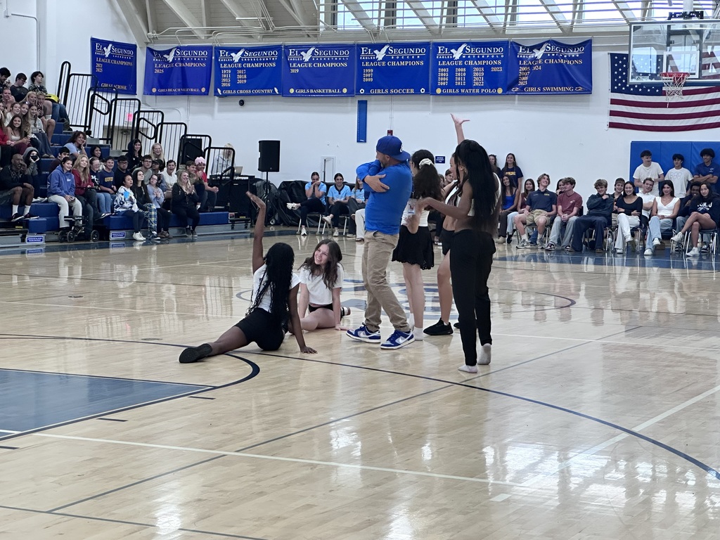 Students and a staff member celebrate on the gym floor, posing and dancing as classmates smile and watch from the bleachers.