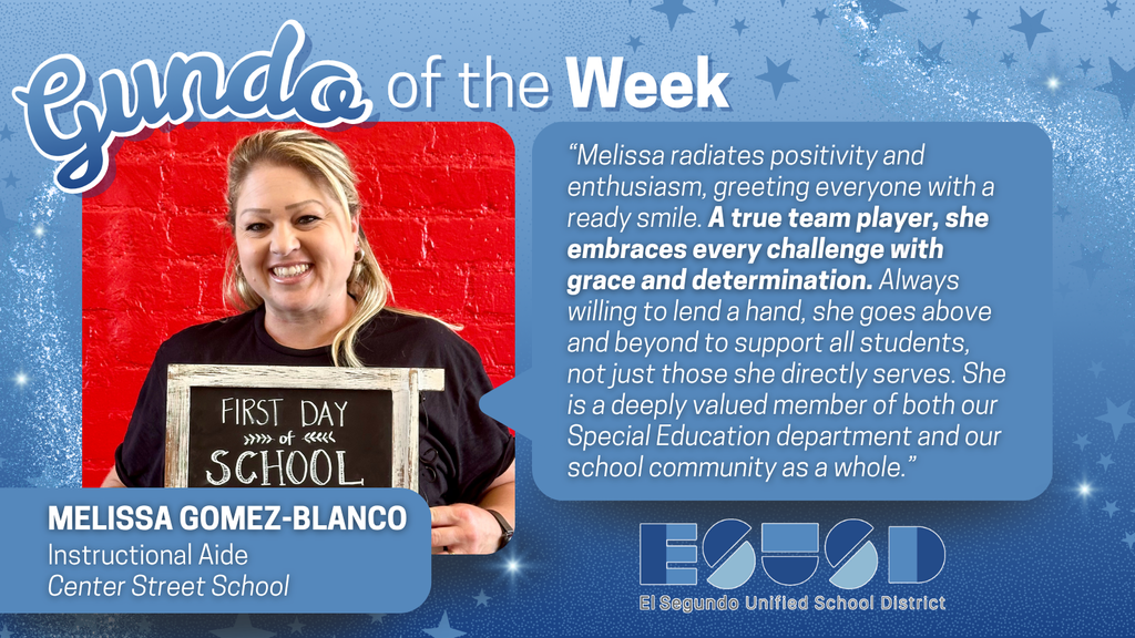 Instructional aide Melissa Gomez-Blanco holds a 'First Day of School' sign against a red brick wall, featured as Gundo of the Week for her positivity and dedication.