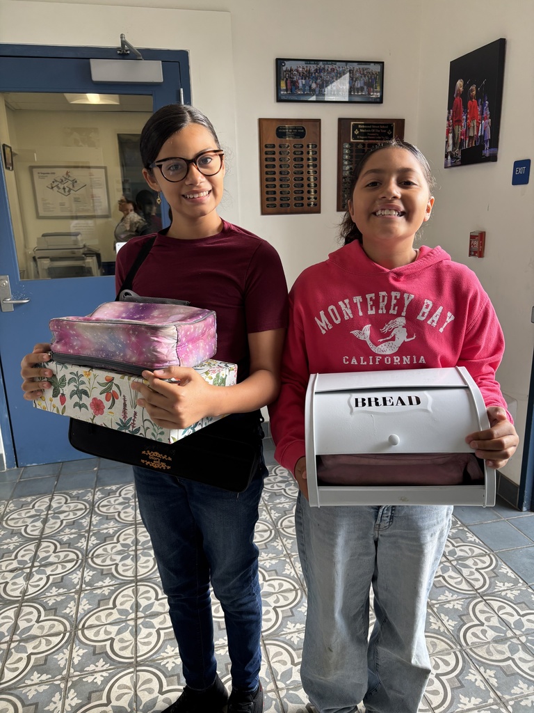 Two people standing indoors holding decorative boxes, one with a floral pattern and the other labeled 'BREAD'.