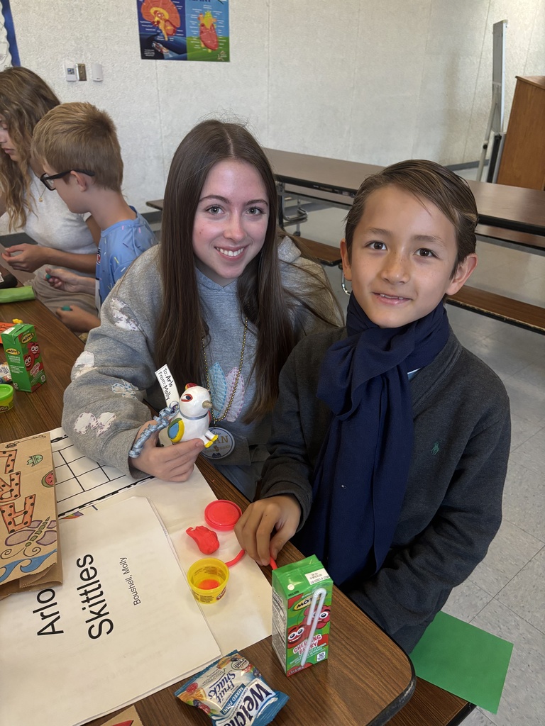 Two children sitting at a table engaged in an arts and crafts activity with colorful materials and juice boxes nearby.
