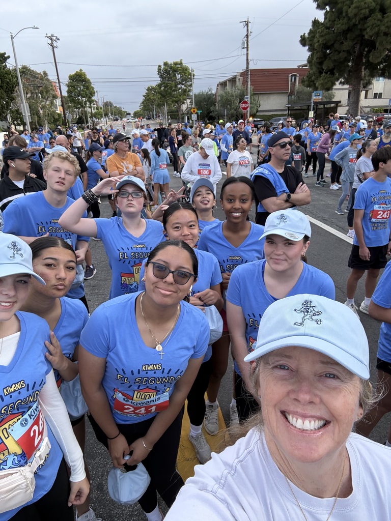 Large group of runners in blue event shirts gathered on a city street before a race start under cloudy skies.