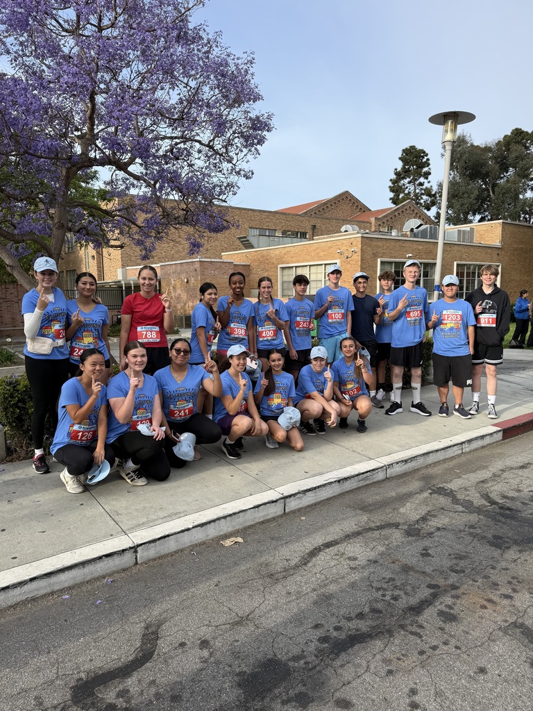 Group of runners in blue shirts posing on a sidewalk after a race near a blooming tree.