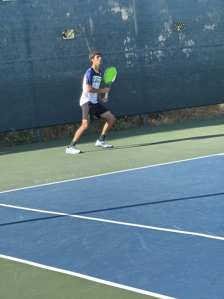 Young male tennis player in mid-action preparing to hit a ball on an outdoor court with a green racket.