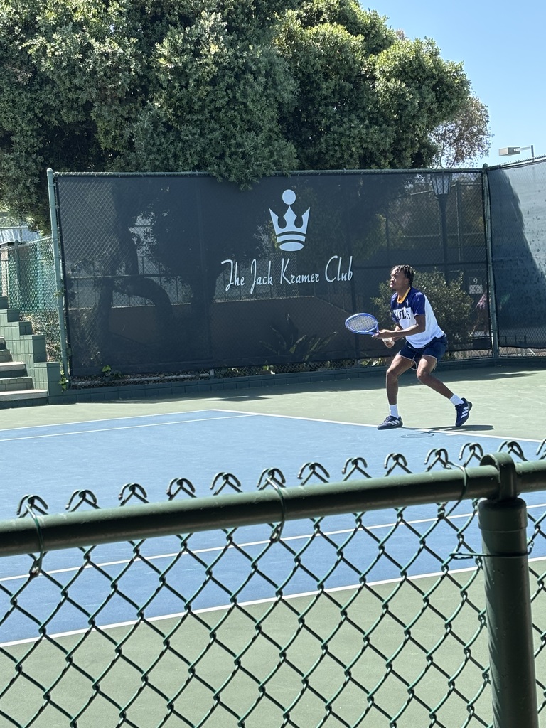 A tennis player in mid-action on a blue court at The Jack Kramer Club, preparing to hit a shot under clear skies.