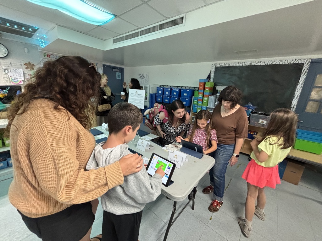Parents and students explore coding activities on tablets in an elementary classroom during open house night.