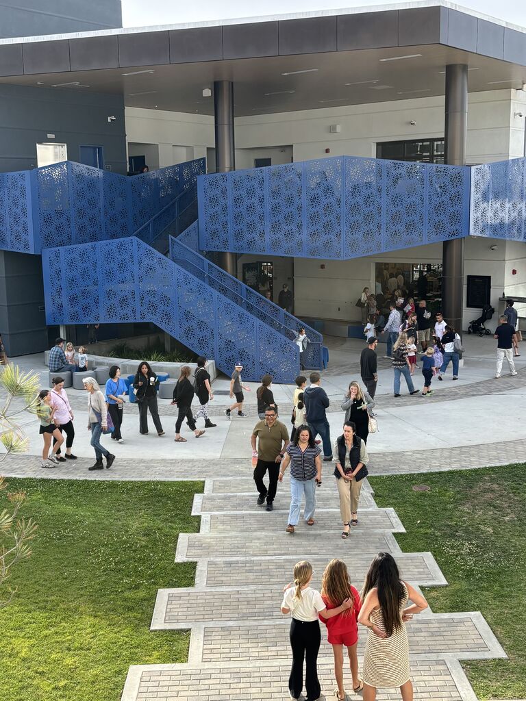 Families walk through a modern school courtyard with blue staircases during an evening campus event.