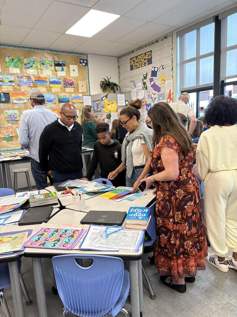 Families review student artwork and projects displayed around an elementary classroom during curriculum night.