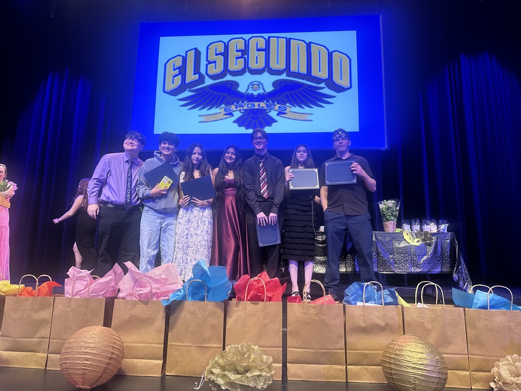 A group of students stand on stage holding certificates and awards during a school recognition ceremony.
