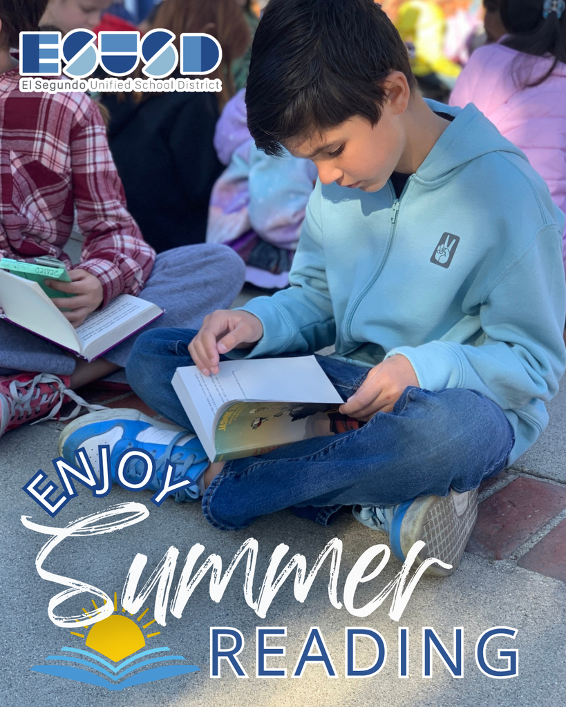 Young student in a light blue hoodie reading a book while seated on a paved surface outside.