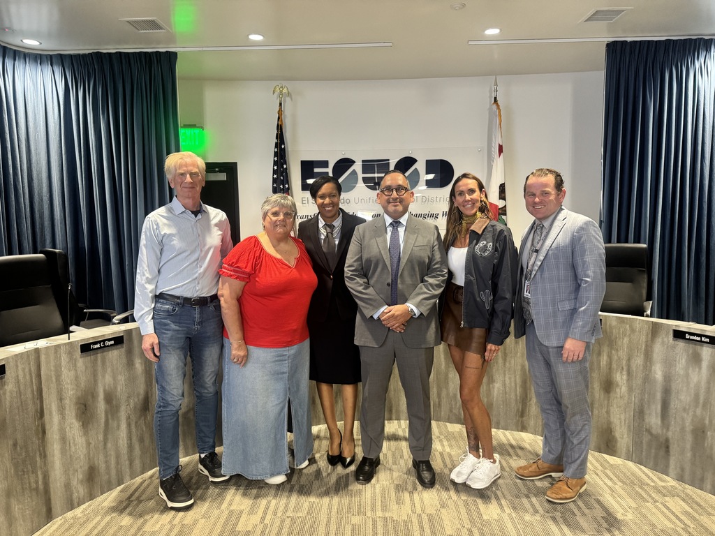 Six diverse individuals standing together in a formal meeting room with the ESCSD logo and American flags behind them.