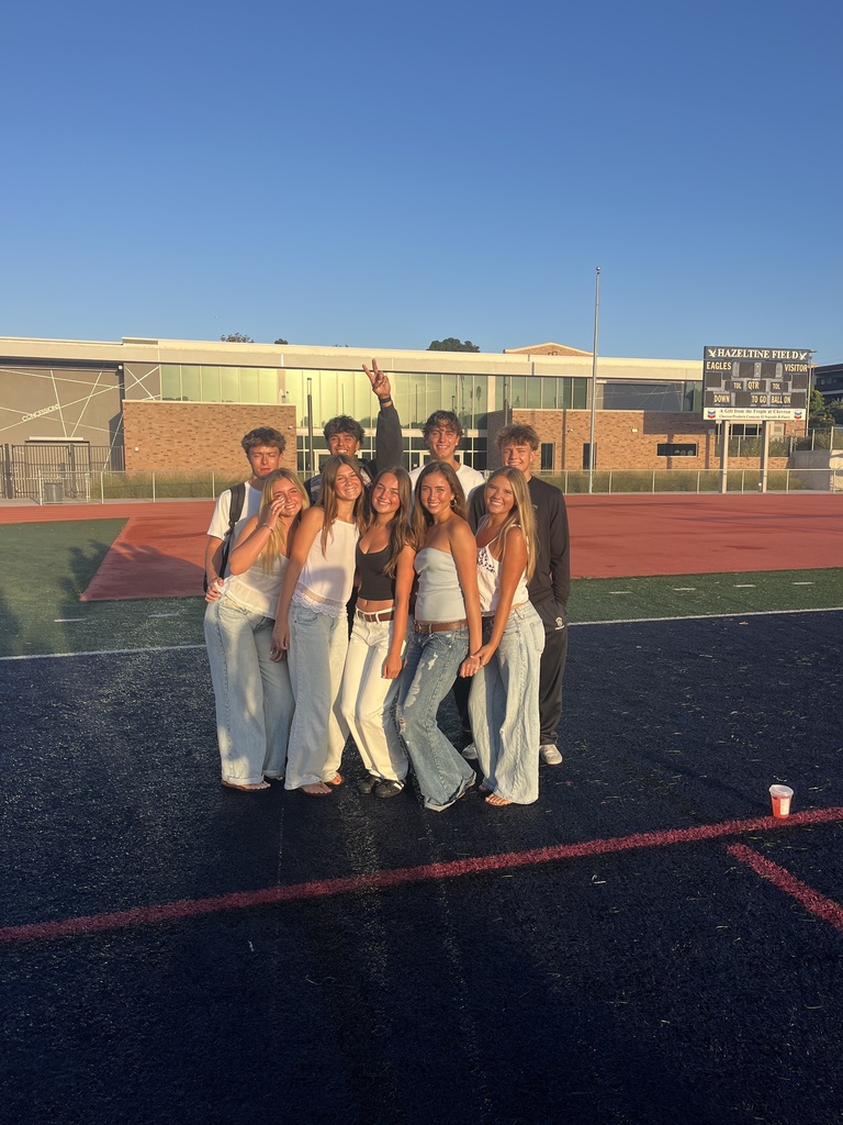 A group of smiling students poses together on a football field in golden morning sunlight.
