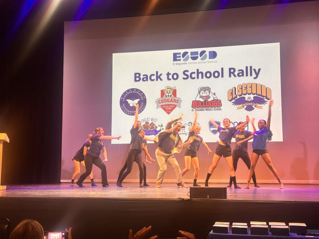 Performers dance onstage beneath a screen announcing the El Segundo Unified School District Back to School Rally.