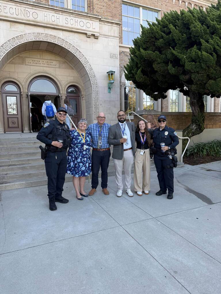 School staff and two police officers pose outside the arched entrance of El Segundo High School.