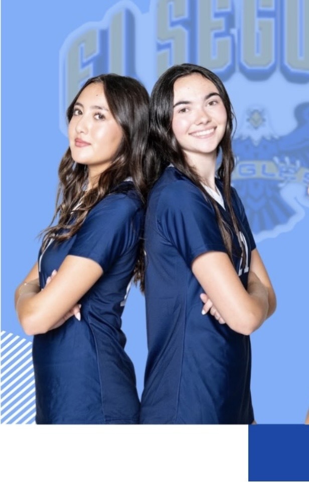 Two young women in navy blue shirts stand back to back, one smiling brightly and the other with a confident expression against a light blue background.