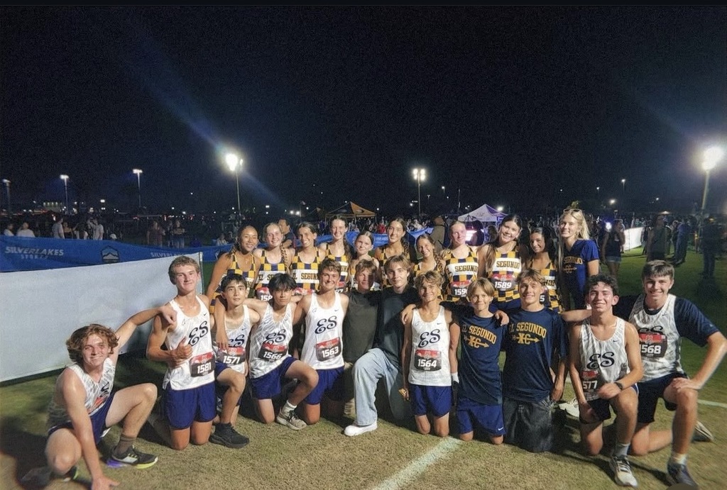 Boys and girls cross-country runners pose together after a nighttime meet under bright stadium lights.