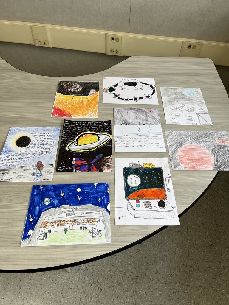 Student artwork depicting space travel, planets, Mars settlements, and futuristic habitats covers a classroom table.