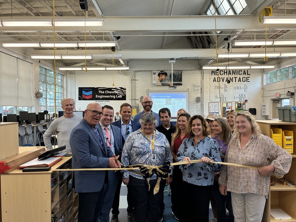 Group of professionals smiling during a ribbon-cutting ceremony inside a bright engineering lab with mechanical tools and equipment.