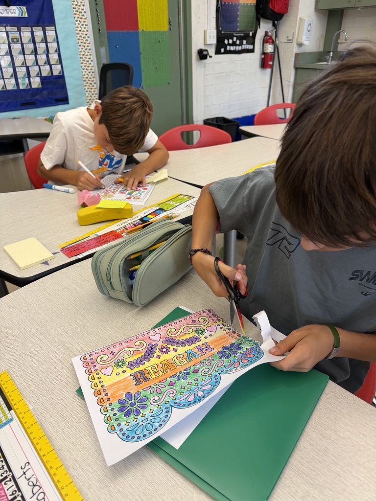 Two boys engaged in arts and crafts at a classroom table, one coloring a detailed floral design while the other cuts out a colorful paper piece.