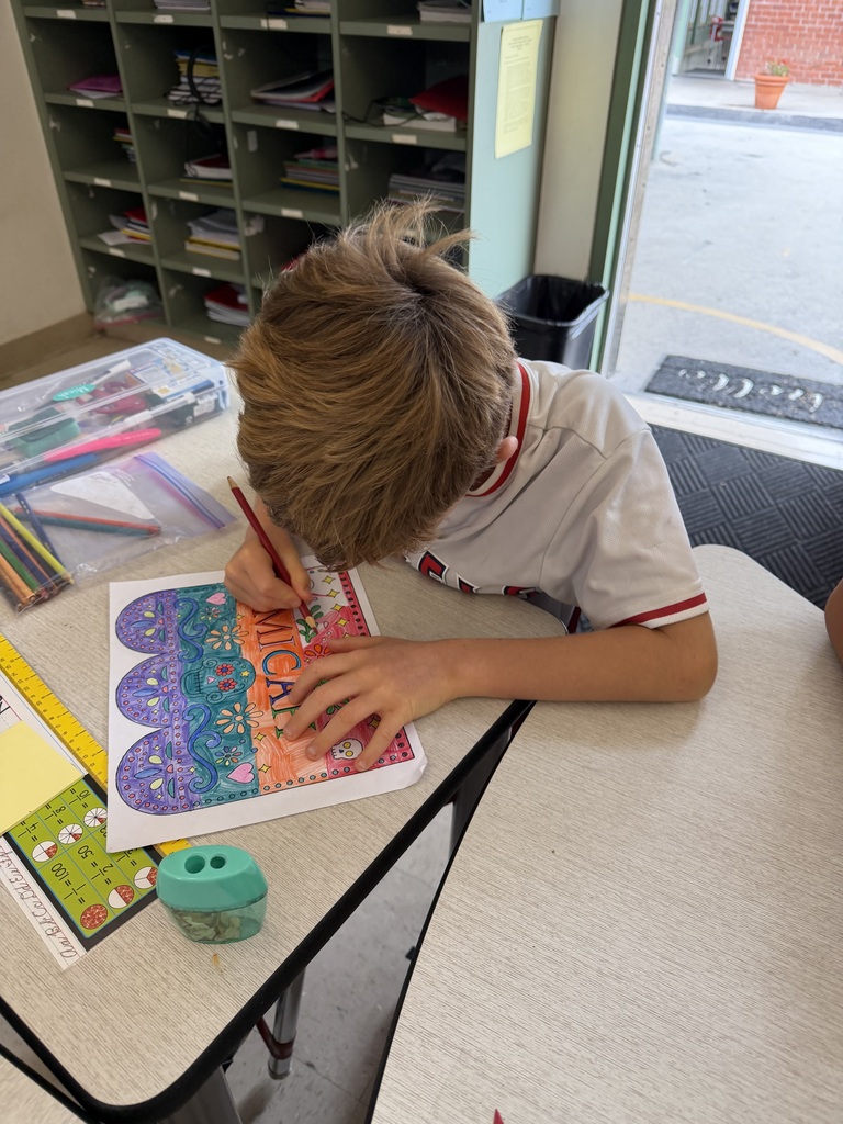 Young boy focused on coloring a detailed mandala design with colored pencils at a classroom desk.