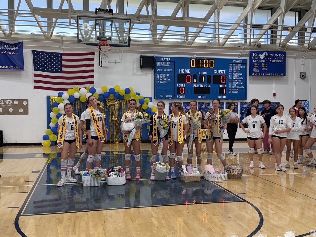 Seven El Segundo High School volleyball seniors pose with flowers and gifts during a Senior Night celebration in the gym.
