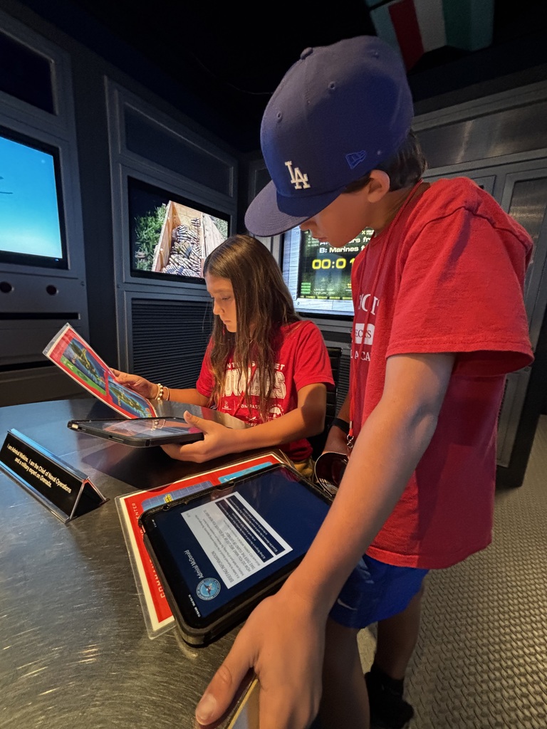 Two students examine tablets and informational materials during an interactive national security simulation.