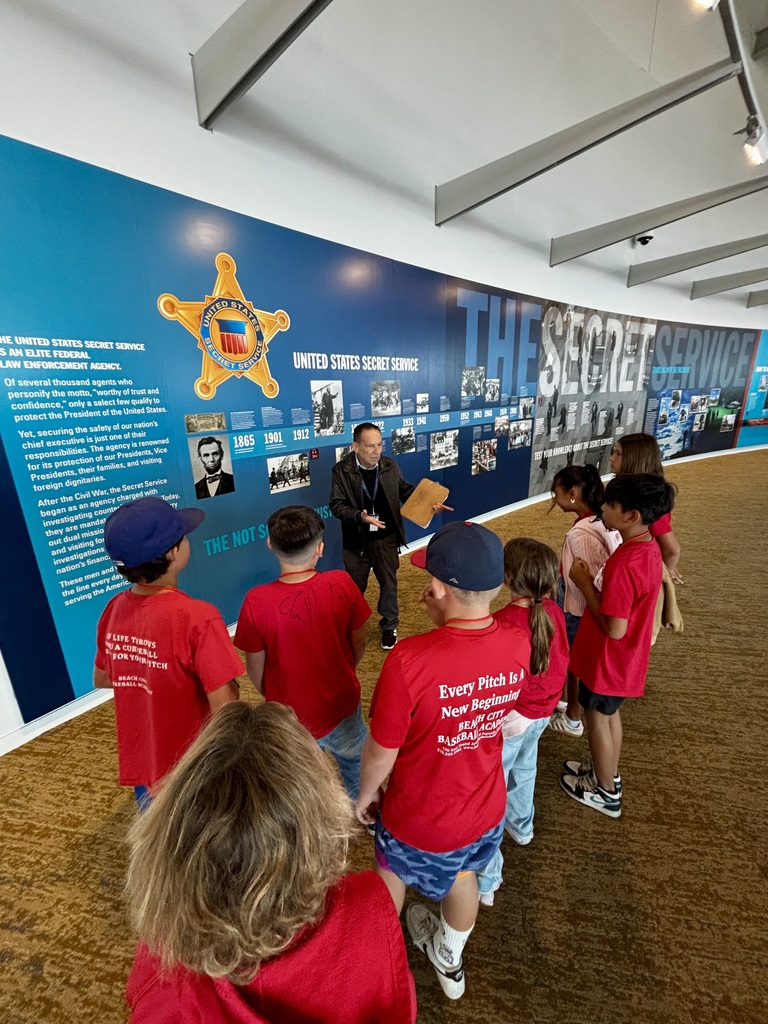 A guide explains Secret Service history to students in red shirts beside a large timeline and historical photo display.