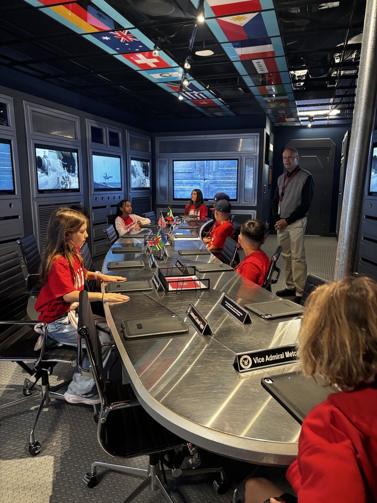 Students explore a simulated government command center with a conference table, digital screens, and international flags.