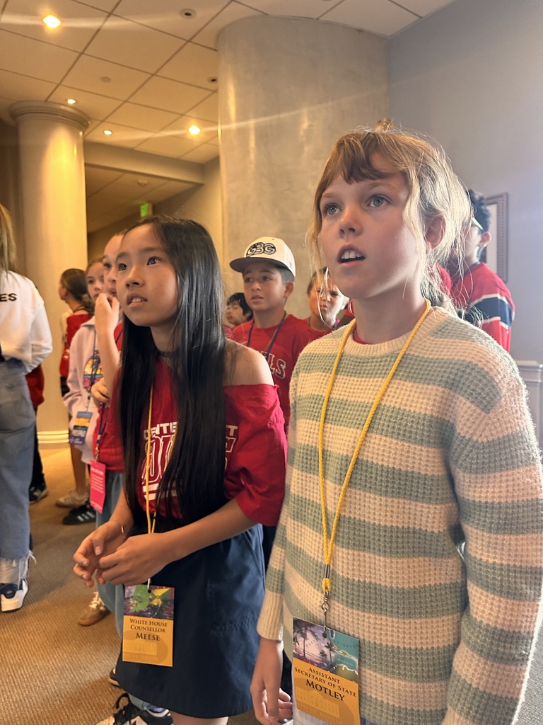 Two students wearing government role badges listen attentively during an educational tour of the White House.