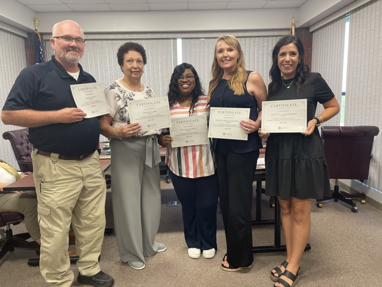 A group of five people standing in front of a table holding certificates