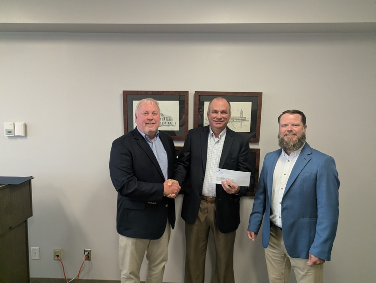 Three men posing for a picture handing off a check.