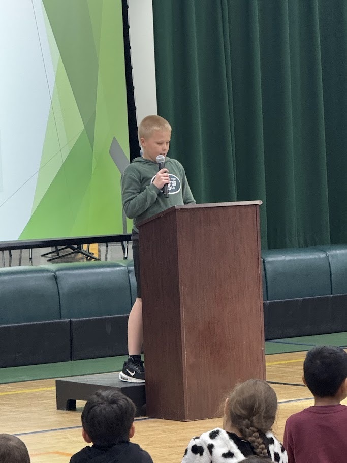 Image of a student speaks into a microphone behind a podium to deliver a speech